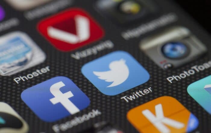 Close-up of a smartphone screen displaying various app icons, including Facebook, Twitter, and other social media and photo apps, on a dark dotted background.