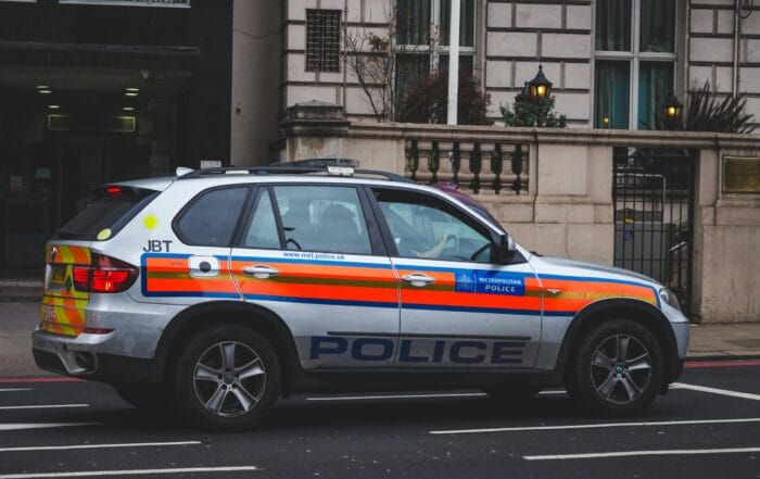 A Metropolitan Police SUV with high-visibility markings is parked on a city street in front of a stone building with large windows and iron gates.