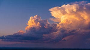 Large, towering clouds lit by golden sunset light against a deep blue sky.