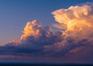 Large, towering clouds lit by golden sunset light against a deep blue sky.