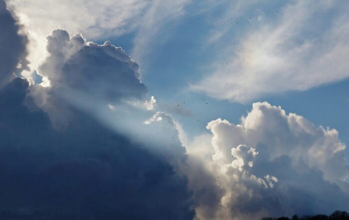 Sunlight breaks through large, dark storm clouds in a blue sky.